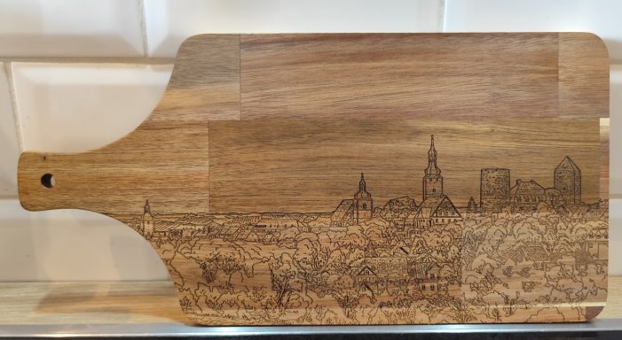 Ein Holzbrett mit eingravierter Skyline einer Stadt, inklusive Gebäuden und Türmen.