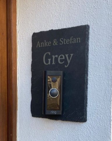 Namensschild aus Stein mit der Aufschrift "Anke & Stefan Grey" und Türsprechanlage.